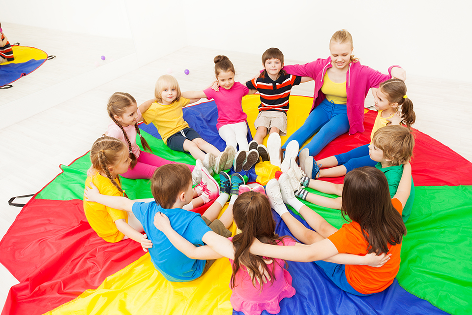 Big group of happy children sitting in a circle with nursery teacher, hugging and playing games